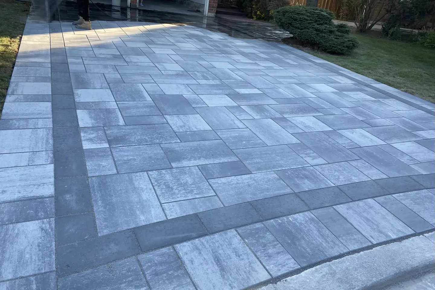 Grey interlock driveway -- large-format pavers, dark charcoal curved border, GTA brick home with double garage